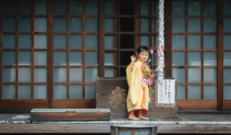 和装した子供の女の子が賽銭の前で手を振っている